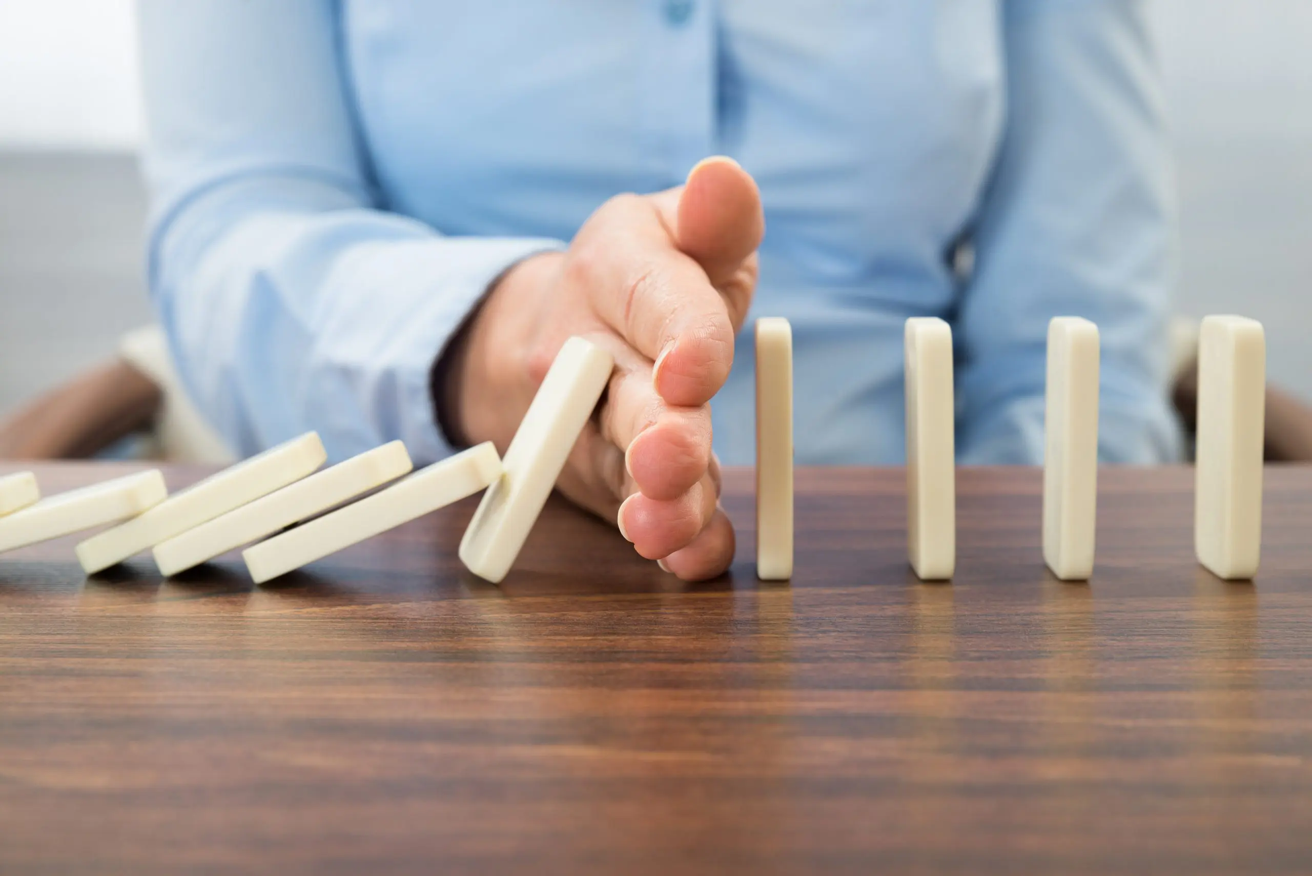 Hand die fallende Dominosteine unterbricht als Symbol für Krisenvermeidung durch Coaching