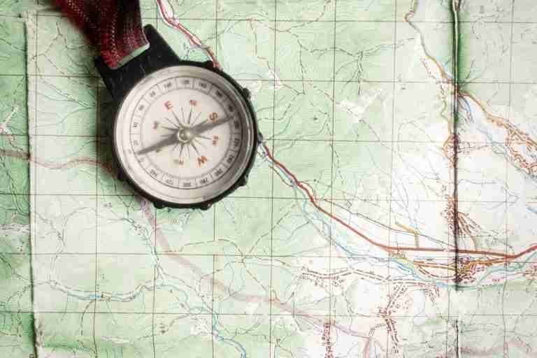 Compass resting on a detailed topographic map with contour lines and trails, ready for navigation.记?