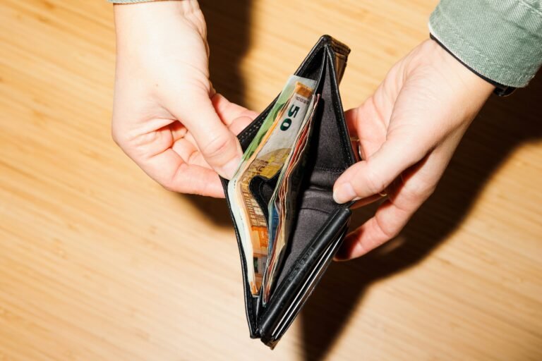 frank-van-hulst-q3BHcWtqqjw-unsplash | Professionelles Coaching in Düsseldorf – Bobach Coaching & Consulting Open black wallet with multiple banknotes visible, held by two hands over a wooden floor background.
