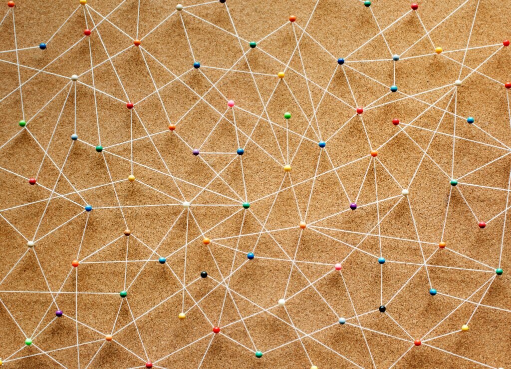 Colorful pins and white strings on a corkboard forming a complex network of connections.