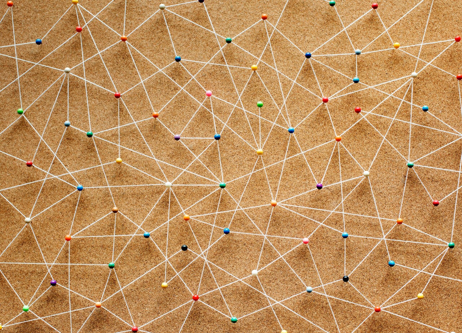 Colorful pins and white strings on a corkboard forming a complex network of connections.